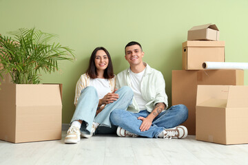 Happy young couple with moving boxes sitting near green wall