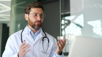 Confident doctor talking on video call using laptop in hospital clinic. Male medical worker physician communicates remotely at conference in office or has an online consultation with patient. Close up