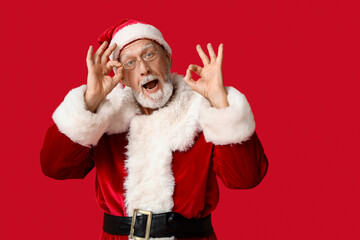 Shocked Santa Claus in glasses showing OK gesture on red background