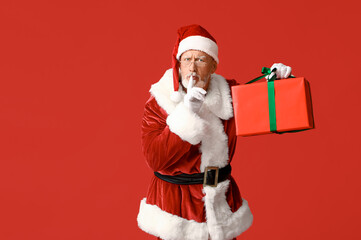Fototapeta na wymiar Santa Claus with gift box showing silent gesture on red background