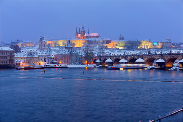 The night snowy Prague Lesser Town with gothic Castle and Charles Bridge above River Vltava, Czech Republic