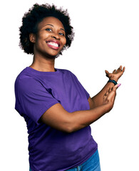 African american woman with afro hair wearing casual purple t shirt inviting to enter smiling natural with open hand