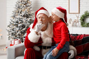 Santa Claus and cute little girl telling her wish on sofa in decorated room for Christmas