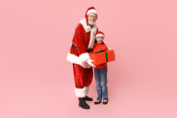 Santa Claus and cute little girl with gift box on pink background