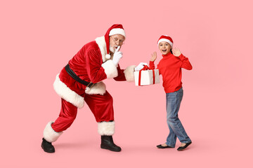 Fototapeta na wymiar Santa Claus and cute little girl with gift box showing silent gesture on pink background