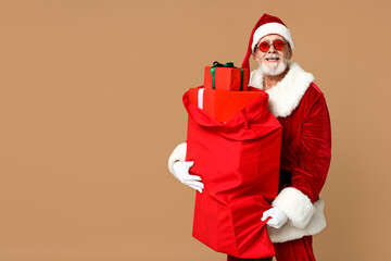 Santa Claus in sunglasses with bag full of gift boxes on brown background