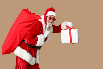 Santa Claus in sunglasses with bag full of gift boxes on brown background