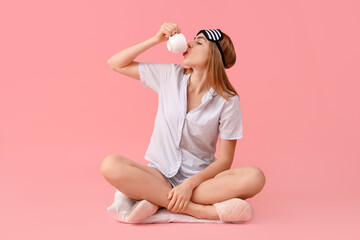 Fototapeta na wymiar Portrait of pretty young woman in pajamas drinking coffee on pink background