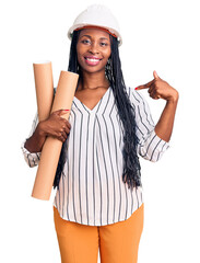 Young african american woman wearing architect hardhat holding blueprints pointing finger to one self smiling happy and proud