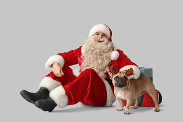 Santa Claus with French bulldog in reindeer horns on grey background