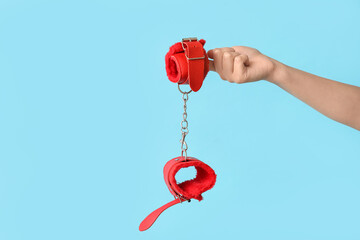 Female hand with handcuffs from sex shop on color background, closeup