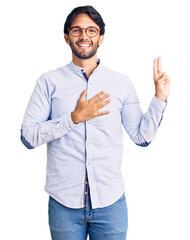 Handsome hispanic man wearing business shirt and glasses smiling swearing with hand on chest and...