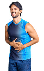 Handsome hispanic man wearing sportswear with hand on stomach because nausea, painful disease feeling unwell. ache concept.