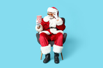 Santa Claus in 3D glasses with bucket of tasty popcorn on blue background