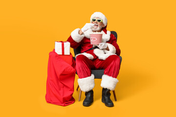 Santa Claus holding bucket of tasty popcorn and bag with gifts on yellow background