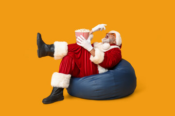 Santa Claus in 3D glasses eating tasty popcorn on yellow background