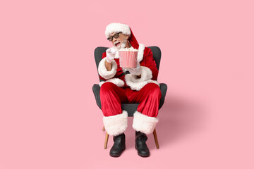 Santa Claus in 3D glasses with bucket of tasty popcorn on pink background