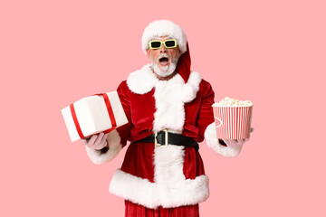 Shocked Santa Claus in 3D glasses with bucket of tasty popcorn and gift box on pink background