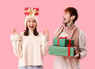 Young couple with Christmas presents on pink background