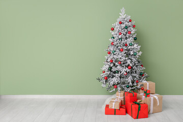 Beautiful decorated Christmas tree with gifts near green wall