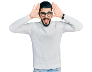 Young arab man with beard wearing elegant turtleneck sweater and glasses smiling cheerful playing peek a boo with hands showing face. surprised and exited