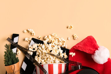 Movie clapper with bucket of popcorn, film reel and Santa hat on beige background