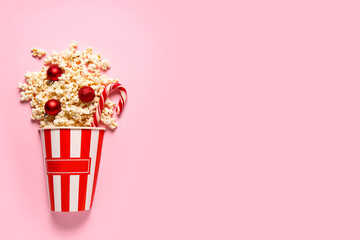 Bucket of popcorn with Christmas tree balls and candy cane on pink background