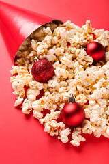 Popcorn with party hat and Christmas tree balls on red background
