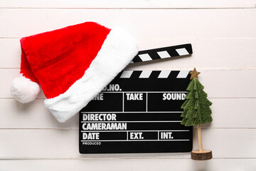 Movie clapper with Santa hat and decorative Christmas tree on white wooden background