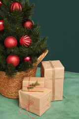 Beautiful Christmas tree in pot with gifts on table against dark green background