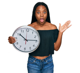 Young african american woman holding big clock celebrating victory with happy smile and winner expression with raised hands