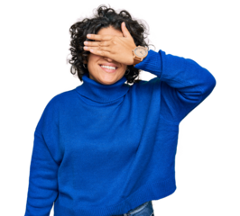 Young hispanic woman with curly hair wearing turtleneck sweater smiling and laughing with hand on face covering eyes for surprise. blind concept.