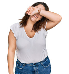 Young plus size woman wearing casual white t shirt covering eyes with arm smiling cheerful and funny. blind concept.