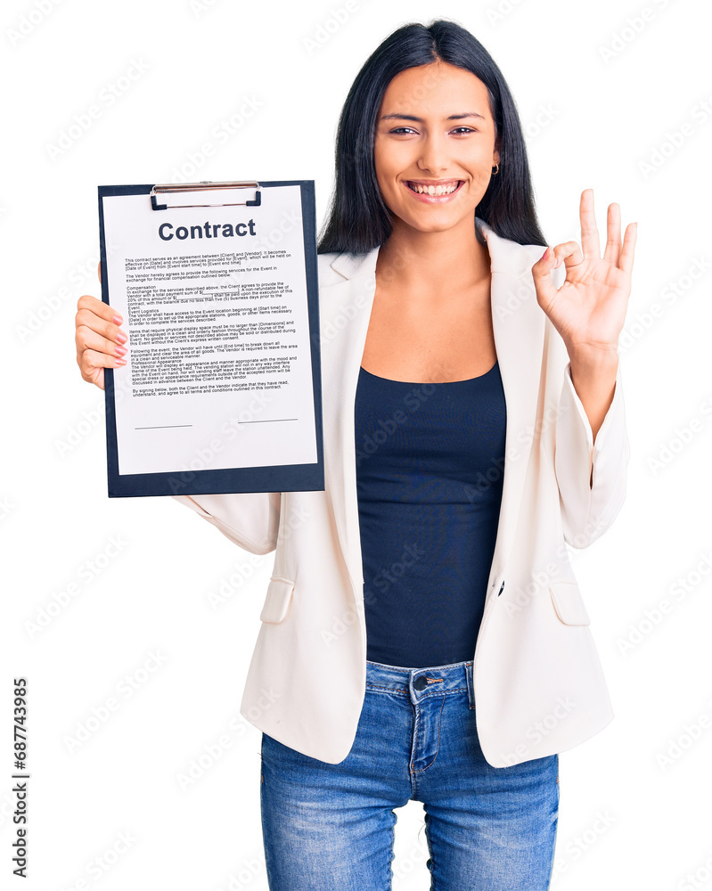 Wall mural Young beautiful latin girl holding clipboard with contract document doing ok sign with fingers, smiling friendly gesturing excellent symbol