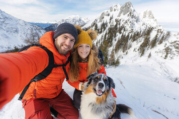 Hiker couple with a dog takes a selfie from a snowy landscape in the winter mountains