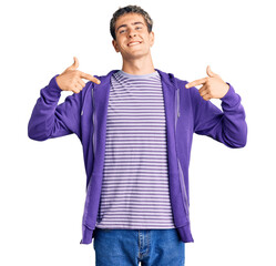 Young handsome man wearing casual purple sweatshirt looking confident with smile on face, pointing...