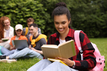 Students learning together in park. Happy woman studying with notebook on green grass, selective...