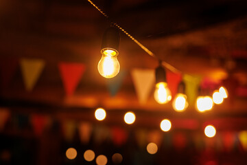 Light bulb hanging from a wire with colorful flags and lights in the background.