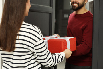Courier giving young woman Christmas gift box indoors, closeup. Sending present by mail