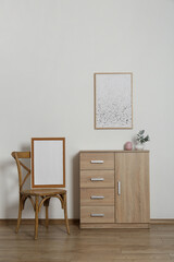 Wooden chair, chest of drawers, vases and frames in room with light wall. Interior design