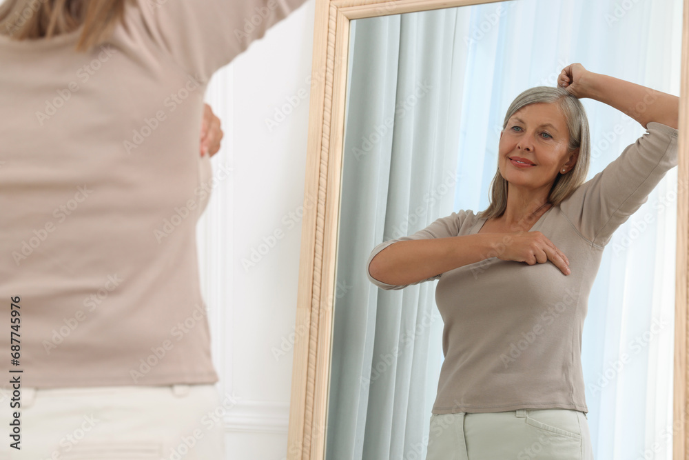 Sticker Beautiful senior woman doing breast self-examination near mirror indoors