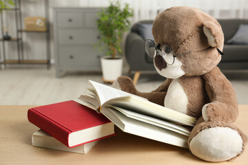 Teddy bear with glasses and open book on wooden table in room, closeup - obrazy, fototapety, plakaty