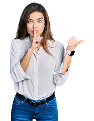 Young caucasian girl wearing casual white shirt asking to be quiet with finger on lips pointing with hand to the side. silence and secret concept.