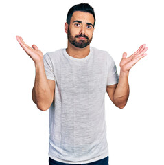 Young hispanic man with beard wearing casual grey t shirt clueless and confused with open arms, no idea and doubtful face. - obrazy, fototapety, plakaty