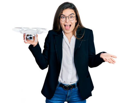 Young caucasian girl wearing business style holding drone celebrating achievement with happy smile and winner expression with raised hand