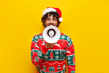 young indian man in new year clothes announces news into megaphone on yellow isolated background