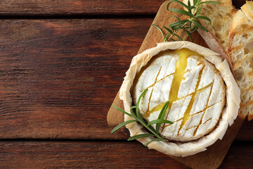 Board with tasty baked brie cheese, bread and rosemary on wooden table, top view. Space for text