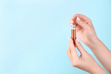 Woman holding bottle of essential oil on light blue background, closeup. Space for text