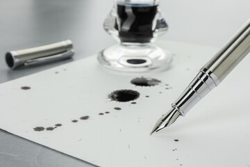 Stylish fountain pen, paper with blots of ink and inkwell on light grey table