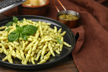 Plate of delicious trofie pasta with pesto sauce and basil leaves on wooden table, closeup. Space...